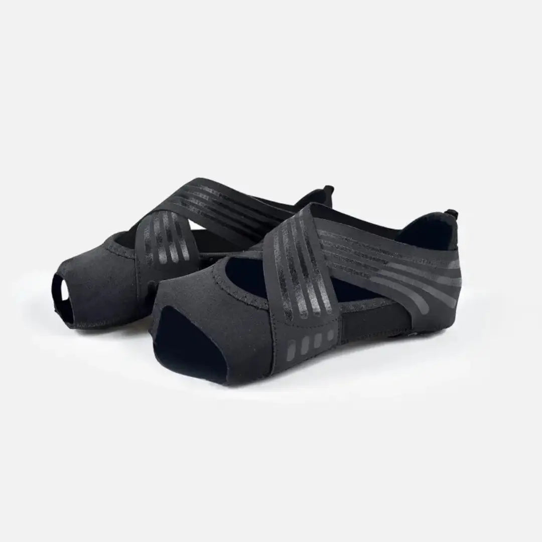 Par de zapatillas elásticas para yoga y pilates color negro entero con bandas cruzadas para soporte.